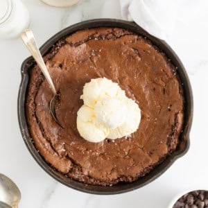 A skillet brownie topped with several scoops of vanilla ice cream.