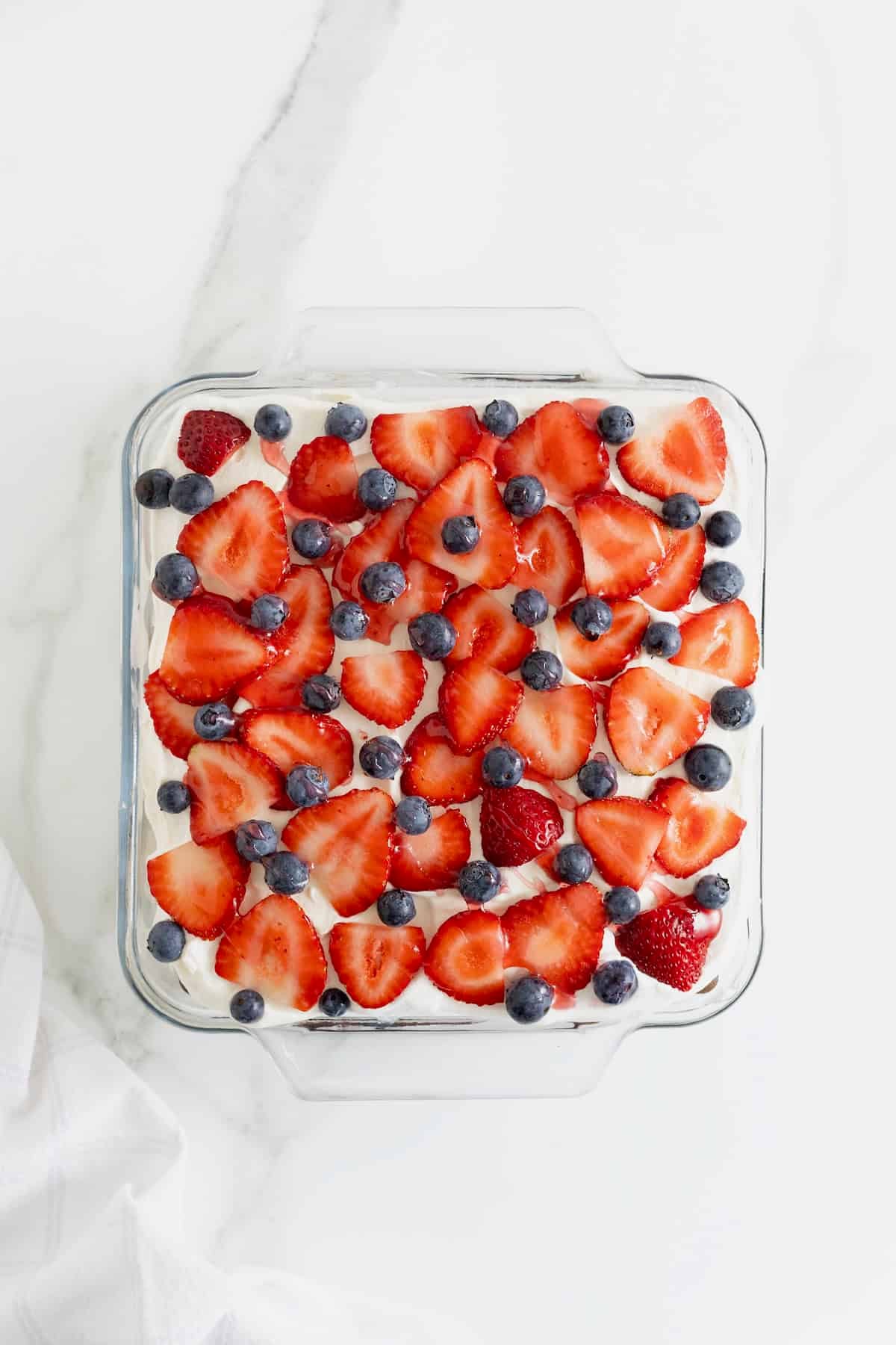 Fresh blueberries, strawberries, and strawberry syrup on an ice cream sandwich cake.