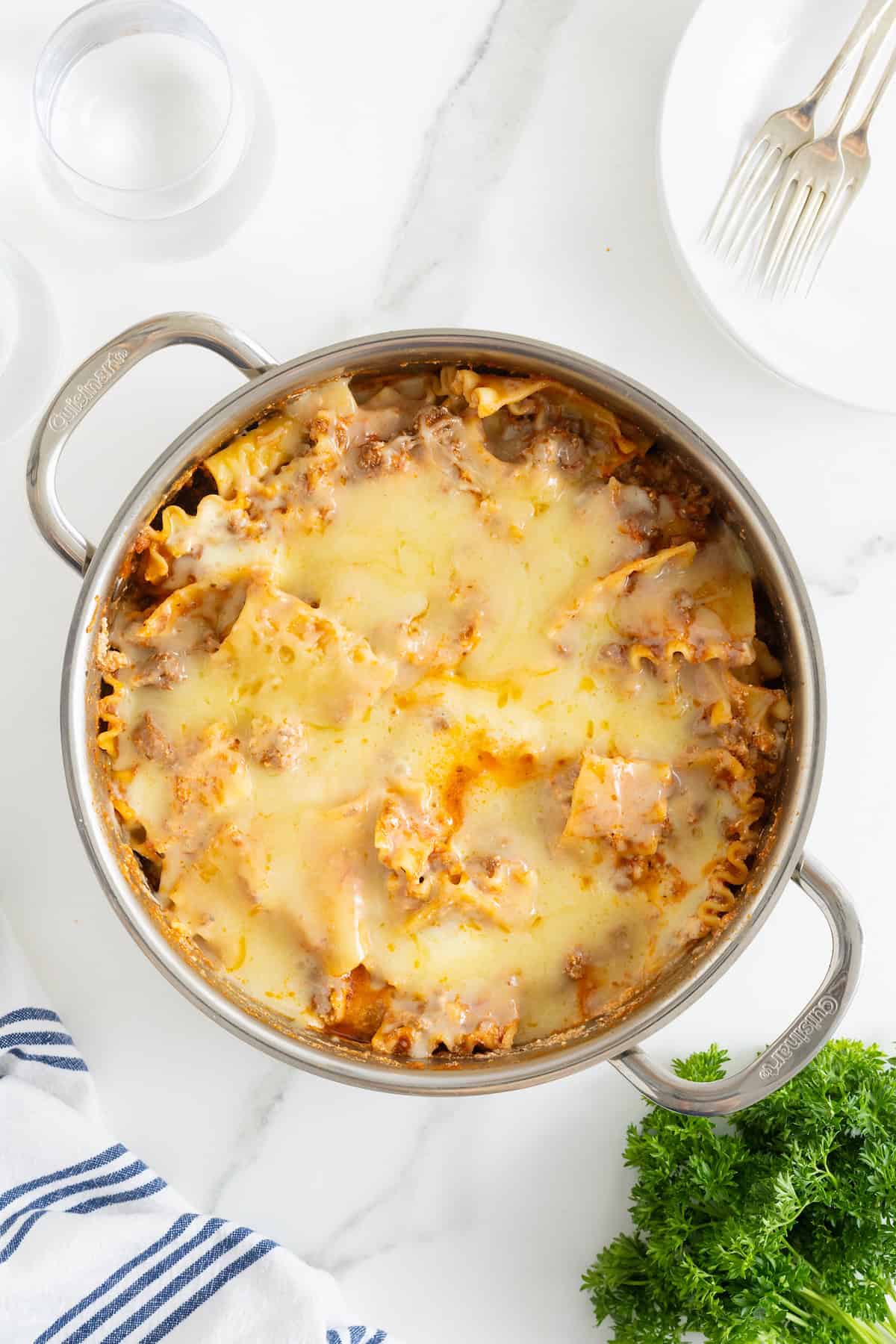 A deep stainless steel skillet with lasagna noodles and melting cheese.