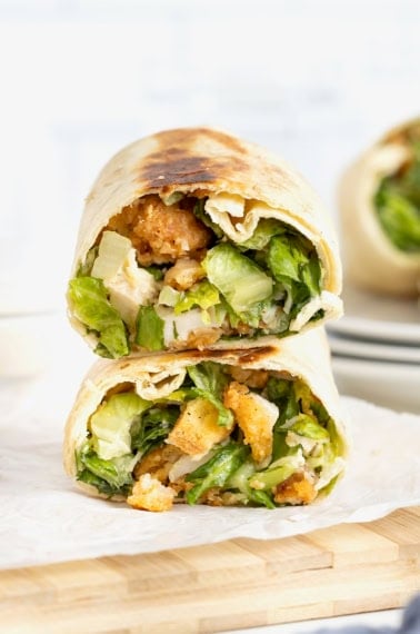 A crispy hot honey chicken caesar wrap cut in half on a parchment lined wood cutting board.