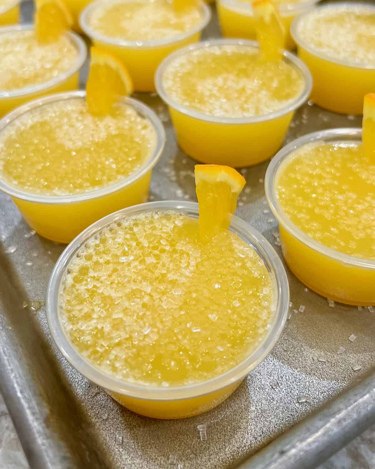 A rimmed aluminum baking sheet filled with mimosa jello shots.