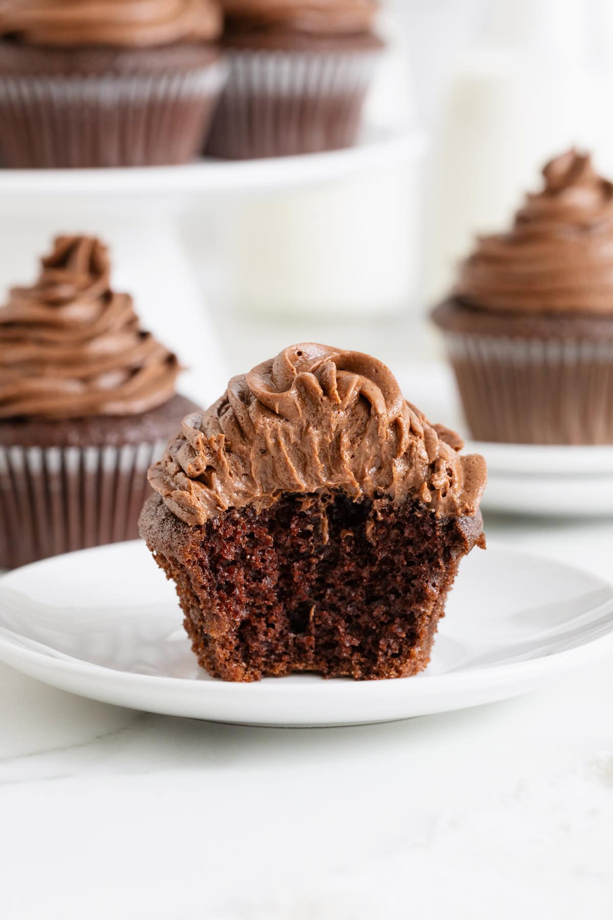 A chocolate cupcake with a bite out of it on a white plate.