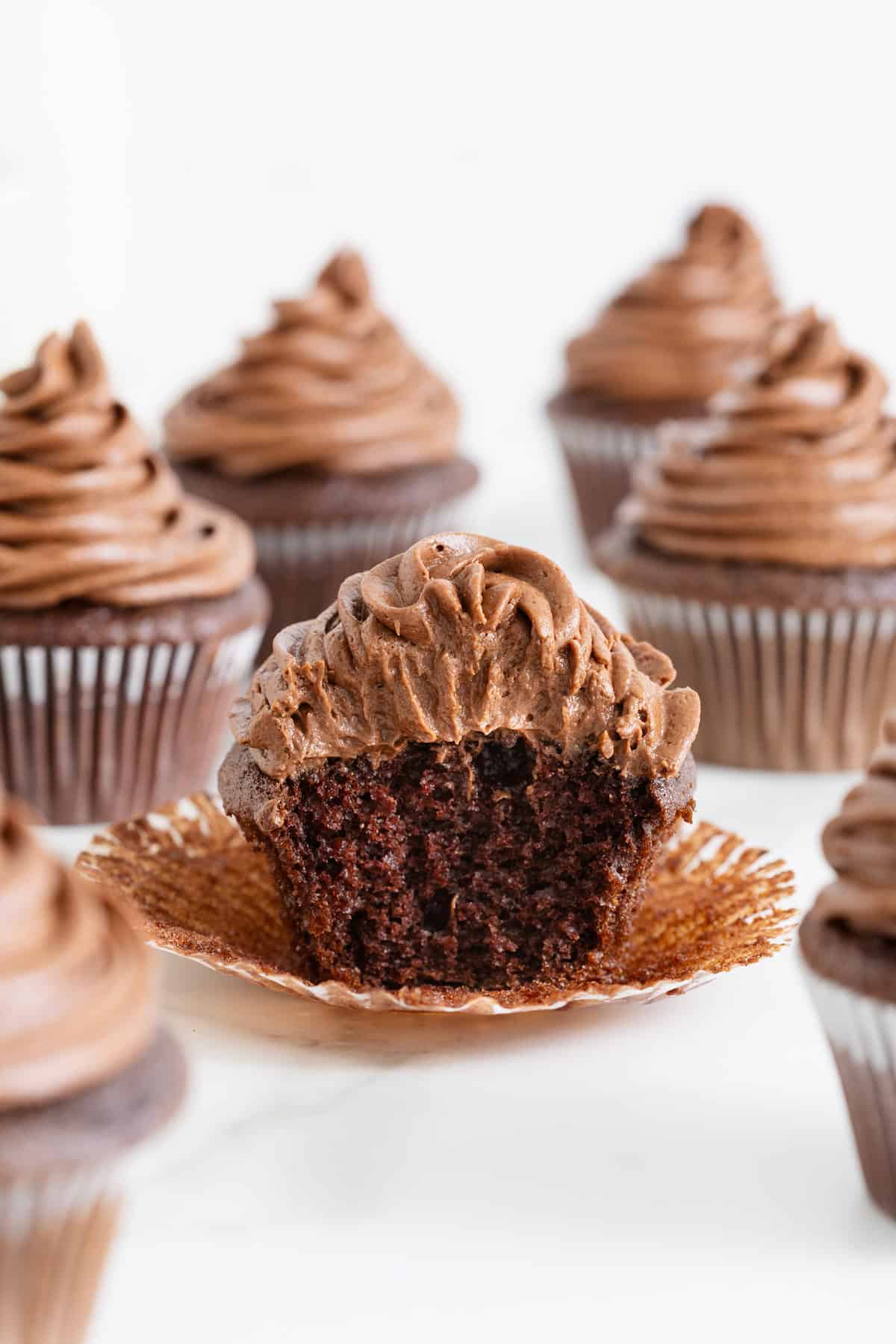 An unwrapped chocolate cupcake with chocolate frosting on a white plate.