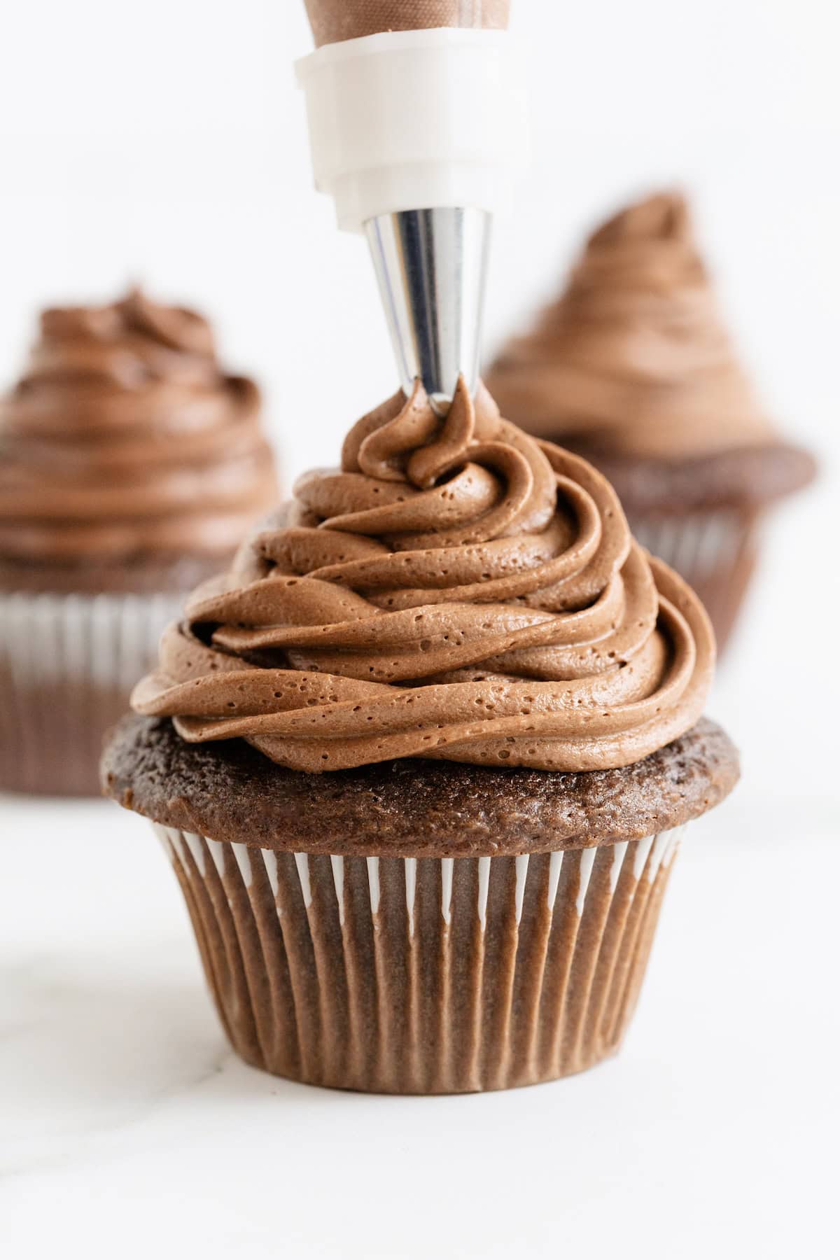 Chocolate buttercream frosting being piped onto a chocolate cupcake.