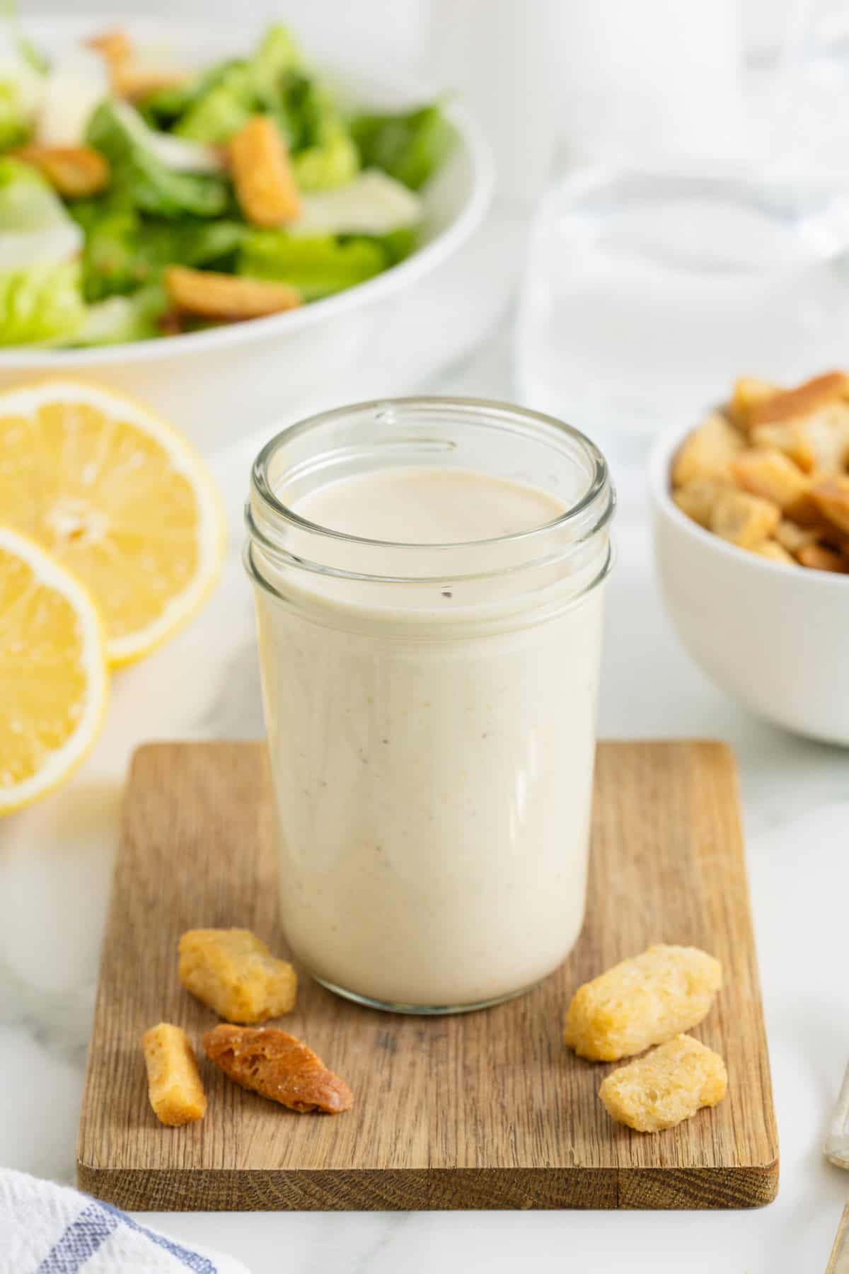 A wide mouth jar of Caesar dressing on a wooden cutting board.