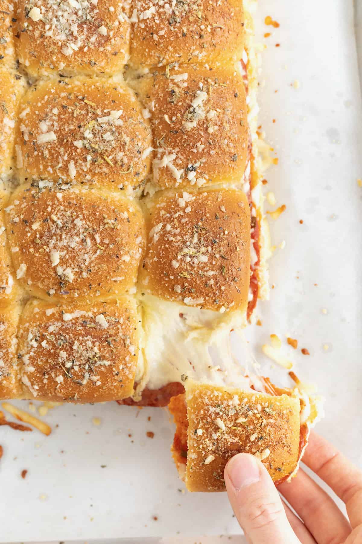 A hand pulling a pizza slider away from the rest of the bunch.