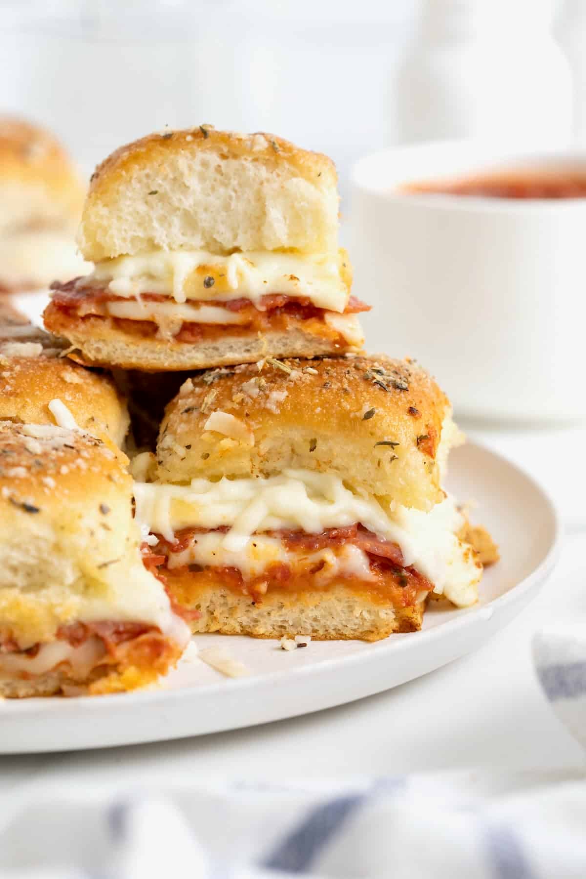 A white platter stacked with pizza sliders.