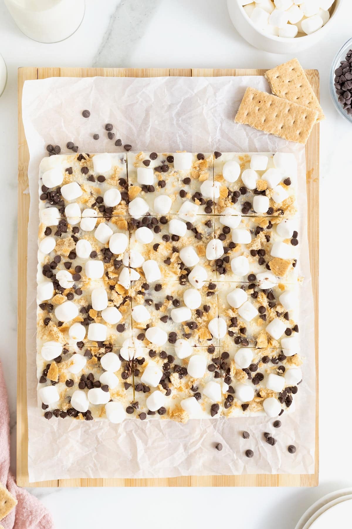 S'mores frozen yogurt bars cut into squares on a parchment lined wood cutting board.