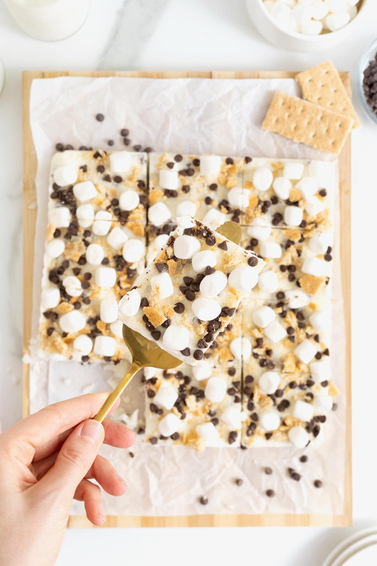 S'mores frozen yogurt bars cut into squares on a parchment lined wood cutting board.