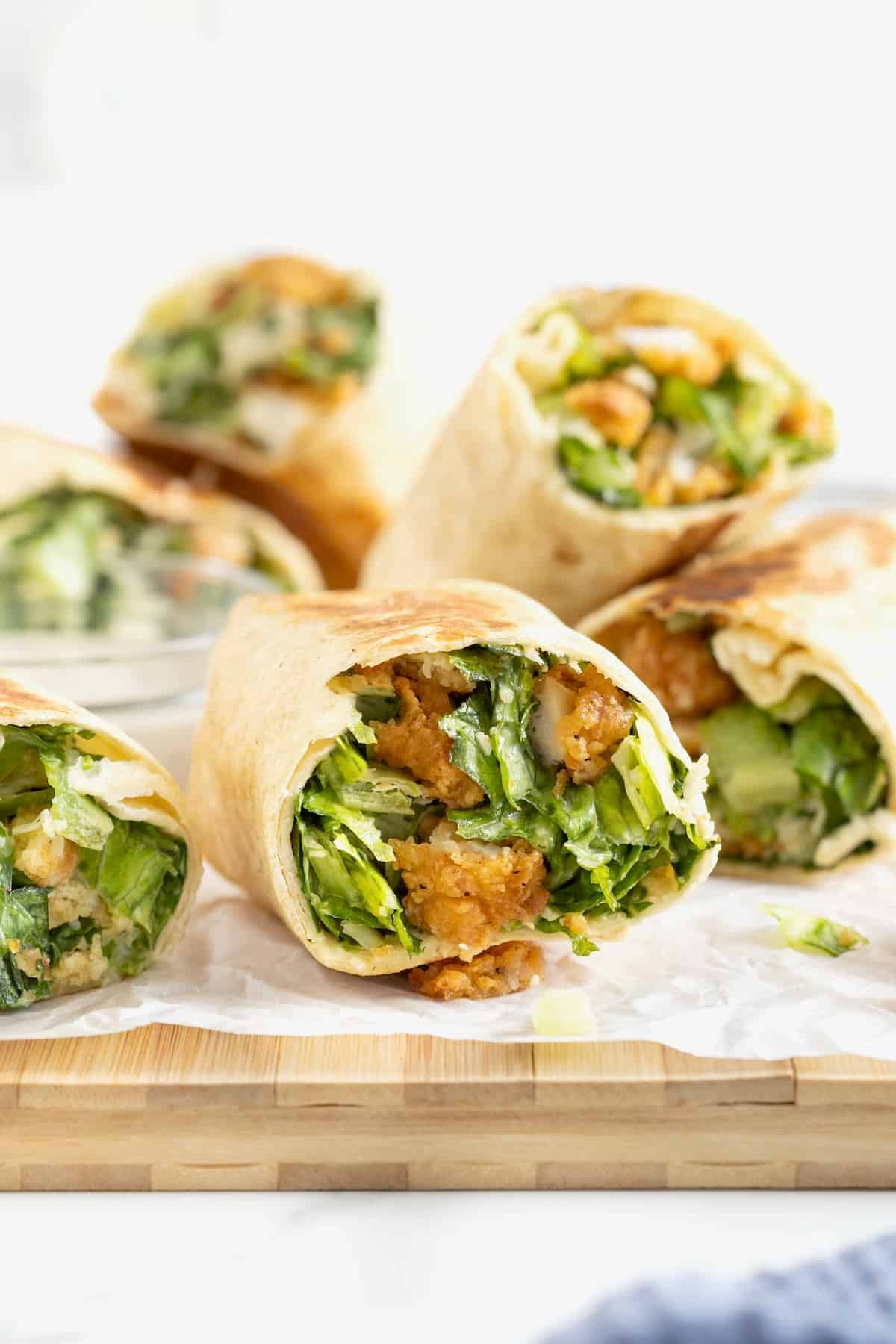 A pile of crispy chicken wraps on a parchment lined wood cutting board.