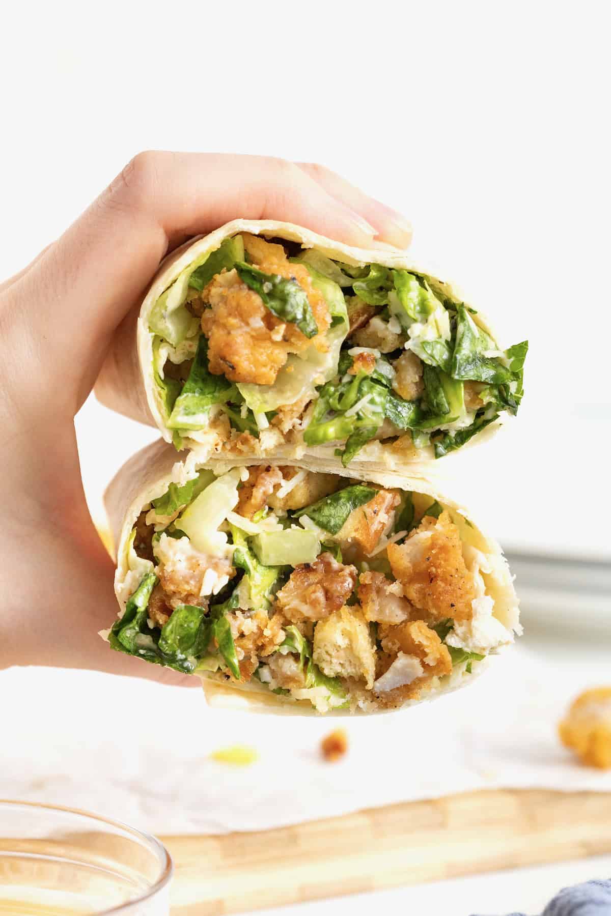 A hand holding two halves of a crispy chicken caesar wrap.