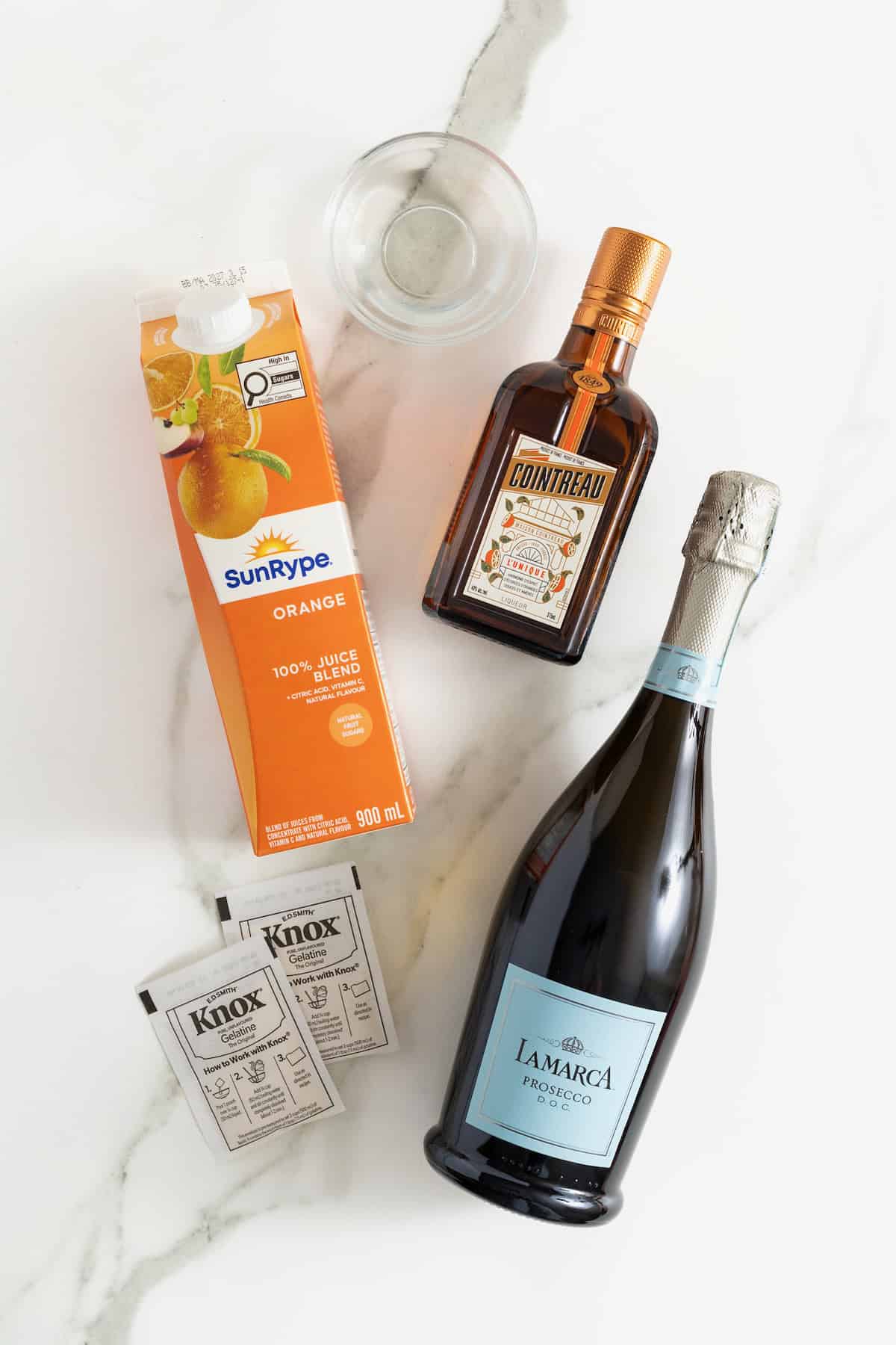 Ingredients to make mimosa jello shots on a white marble counter.