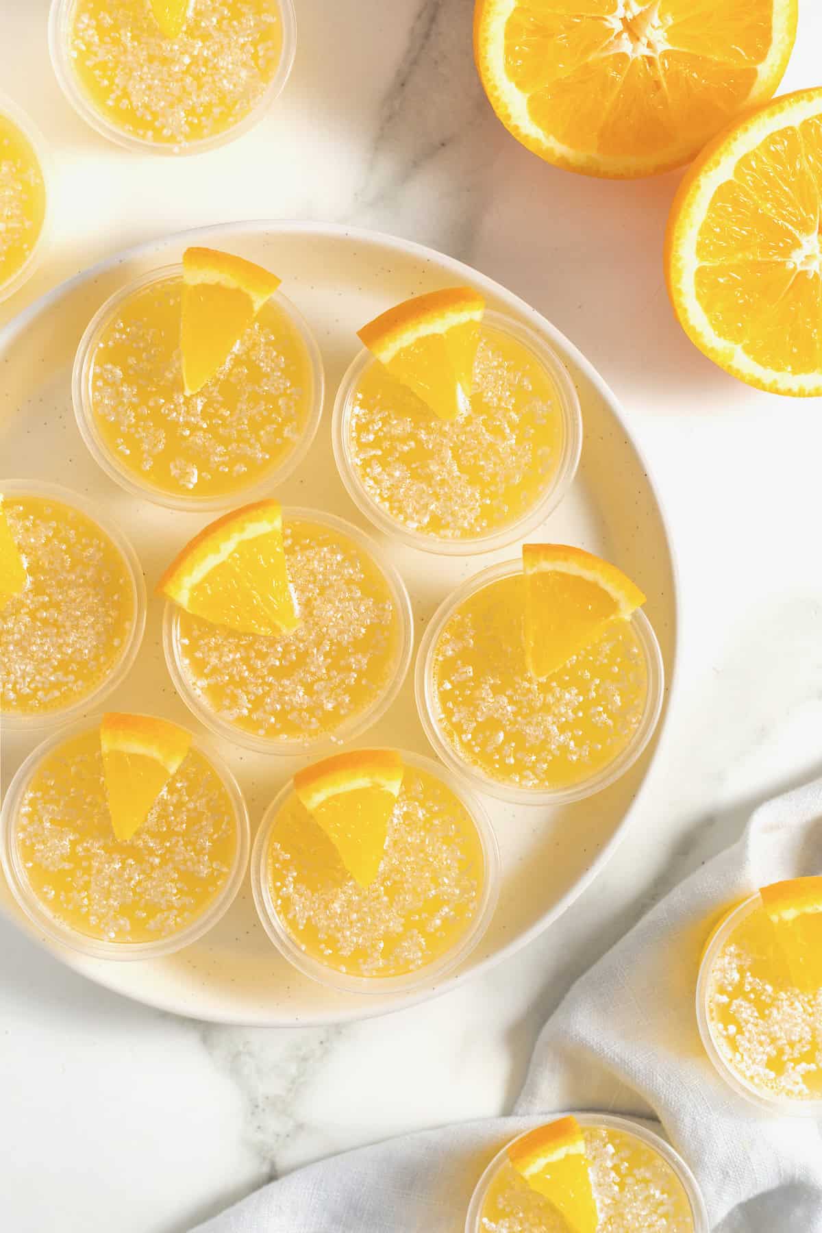 Seven mimosa jello shots in plastic shot cups rimmed in sugar and garnished with a small orange wedge.