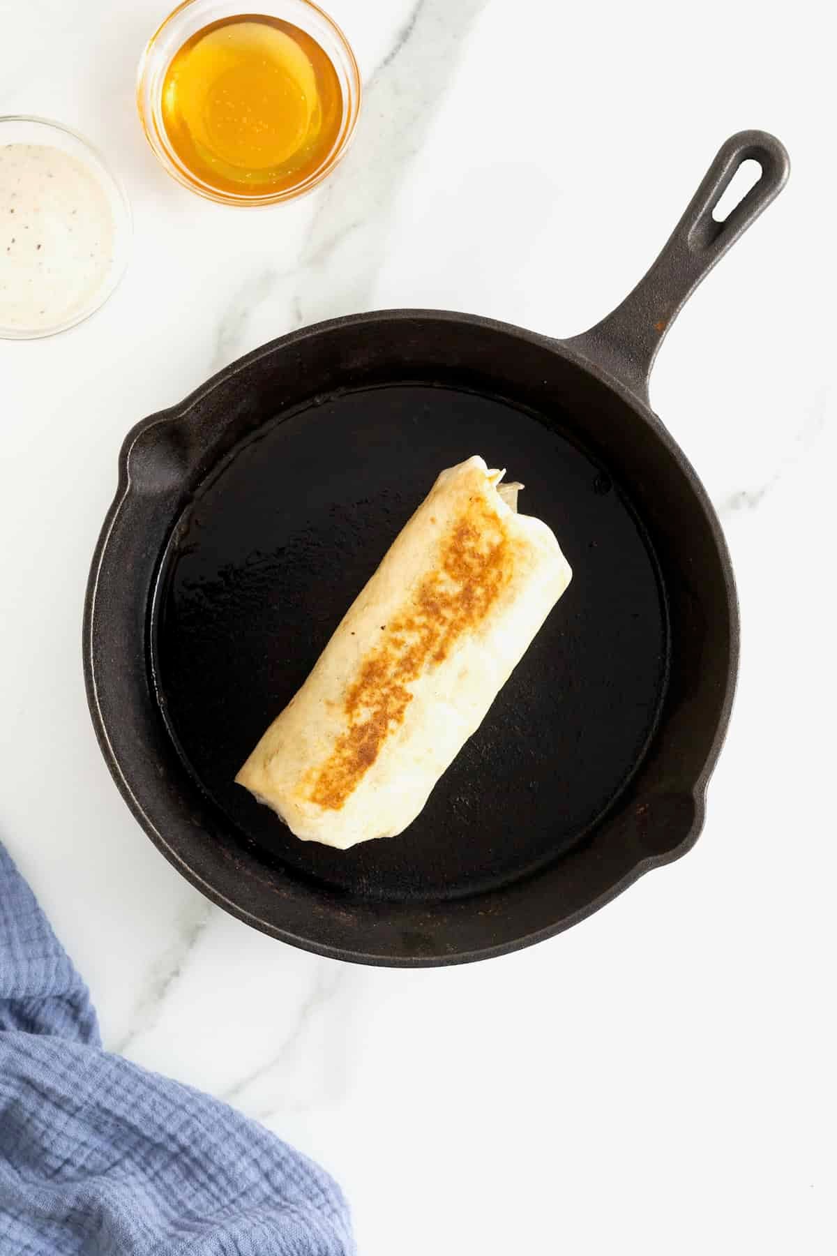 A hot honey chicken caesar wrap toasting in a cast iron skillet.