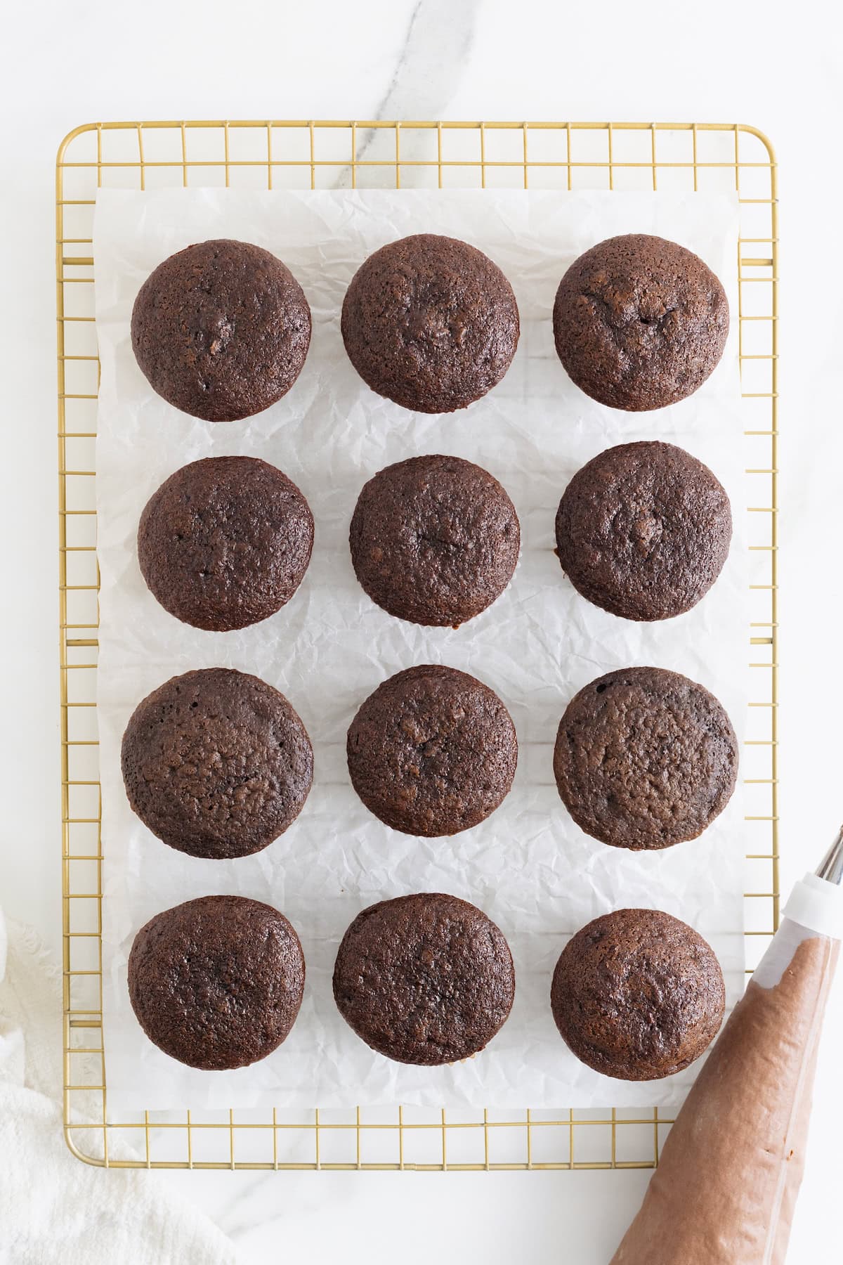Unfrosted chocolate cupcakes on a parchment lined gold toned cooling rack.