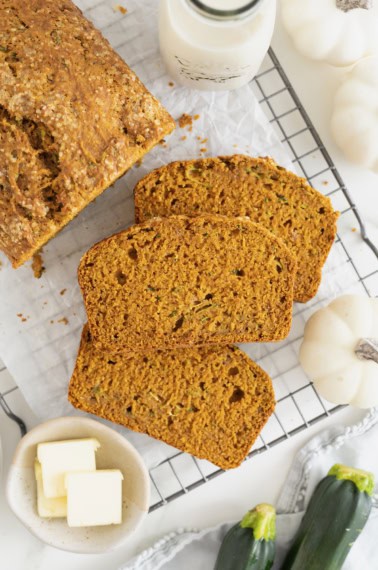 Three slices of whole wheat pumpkin zucchini bread next to the loaf on a parchment lined cooling rack.