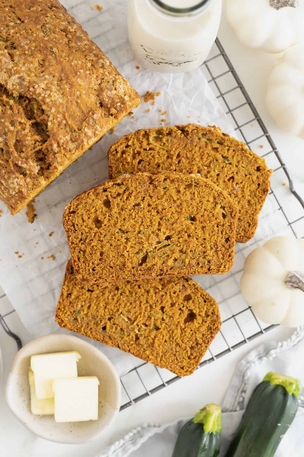 Three slices of whole wheat pumpkin zucchini bread next to the loaf on a parchment lined cooling rack.