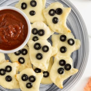 A gray plate piled with ghost shaped tortilla pizzas and a small white dish of marinara sauce.