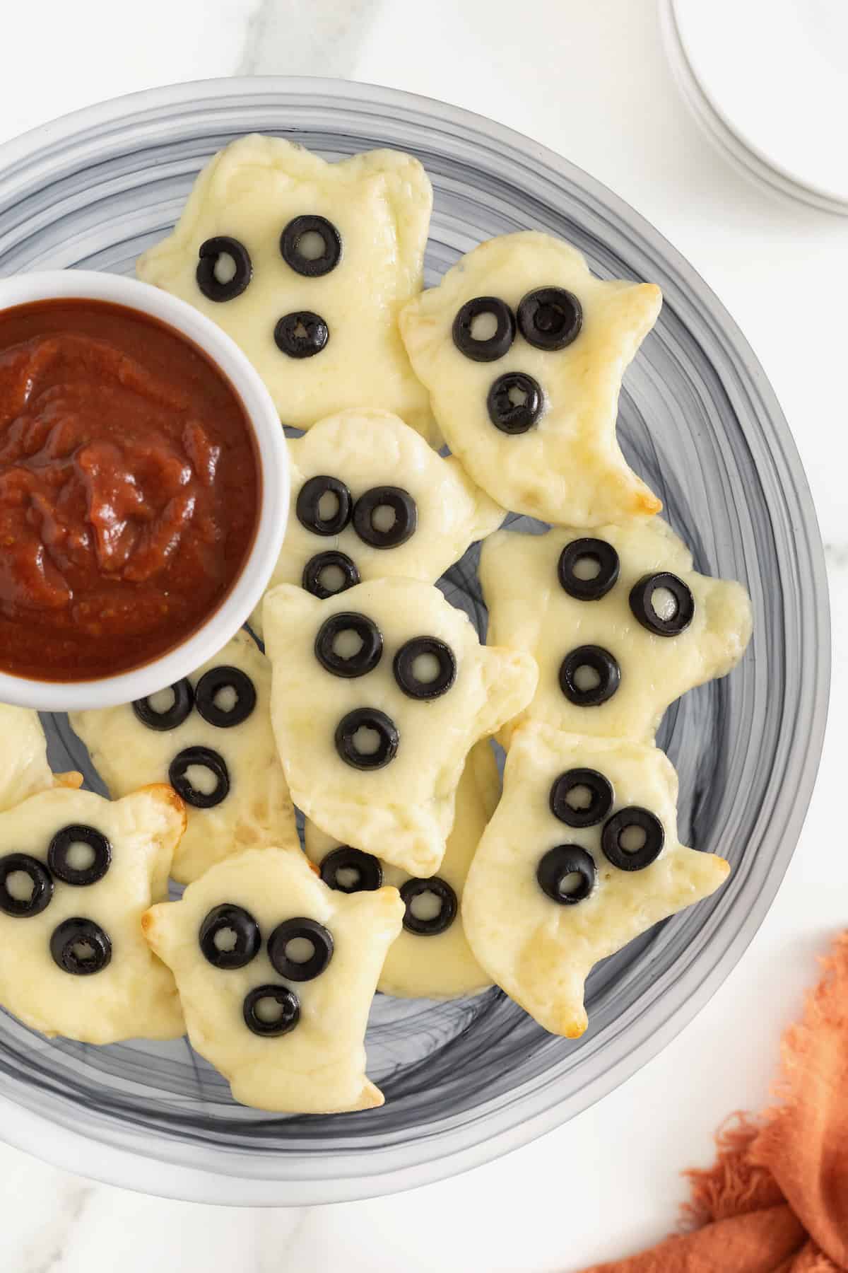 A gray plate piled with ghost shaped tortilla pizzas and a small white dish of marinara sauce.
