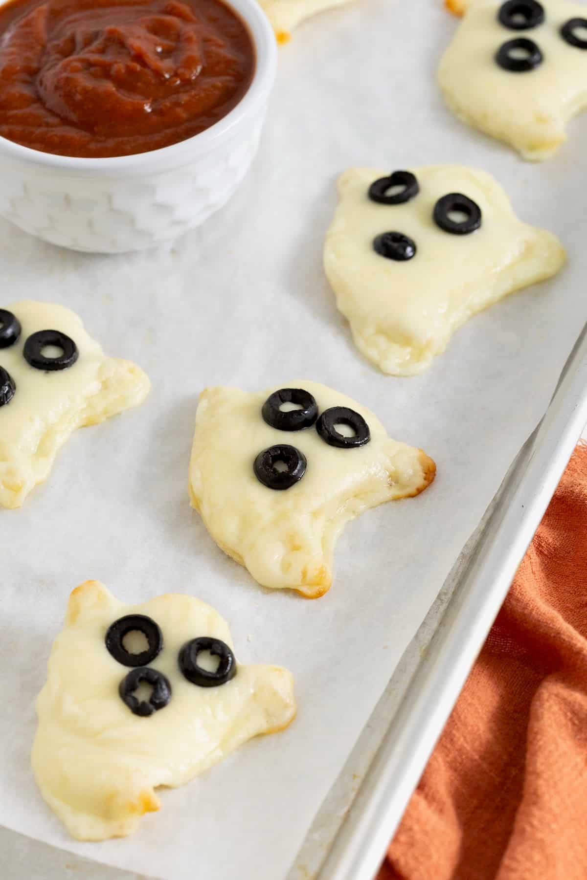 12 ghost shaped tortilla pizzas on a parchment lined baking sheet.