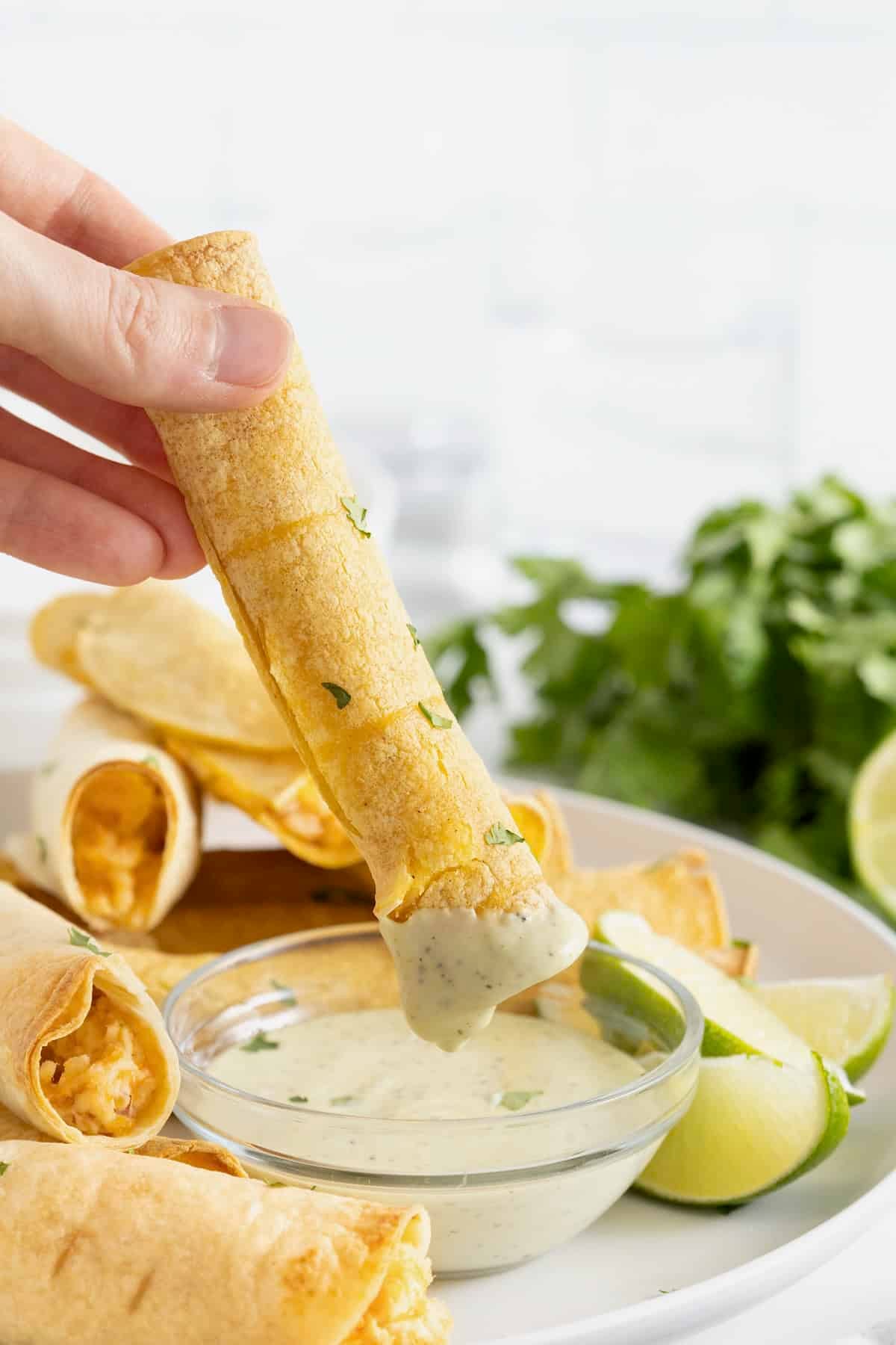 A hand dipping a chicken bacon ranch taquito into cilantro lime ranch.
