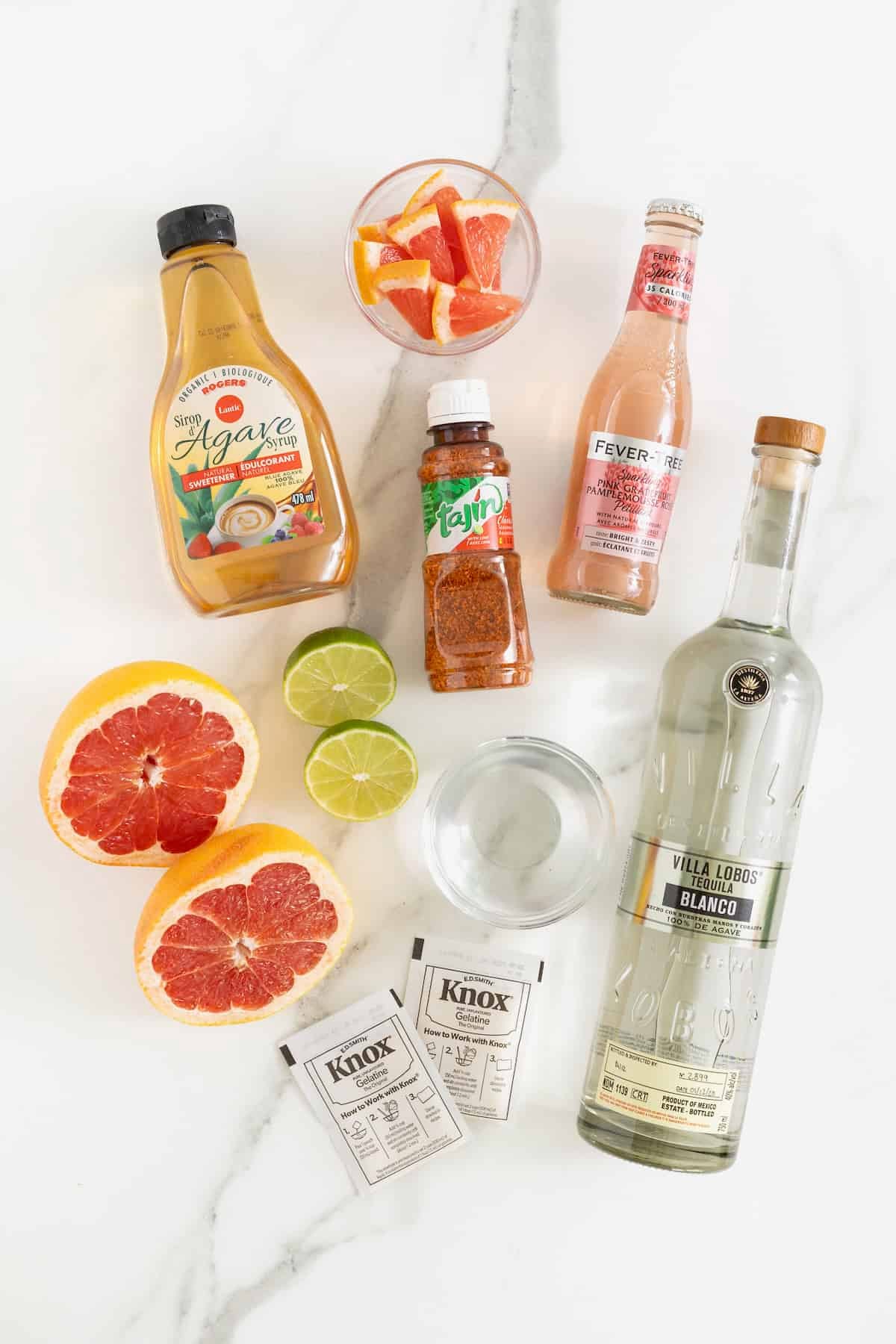 Ingredients to make Paloma jello shots on a white marble counter.