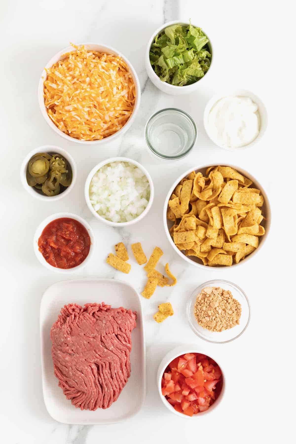 Ingredients to make sheet pan walking tacos in small glass dishes on a white marble counter.