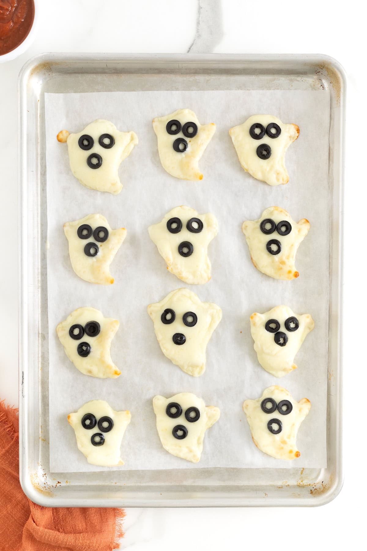 12 ghost shaped tortilla pizzas on a parchment lined baking sheet.