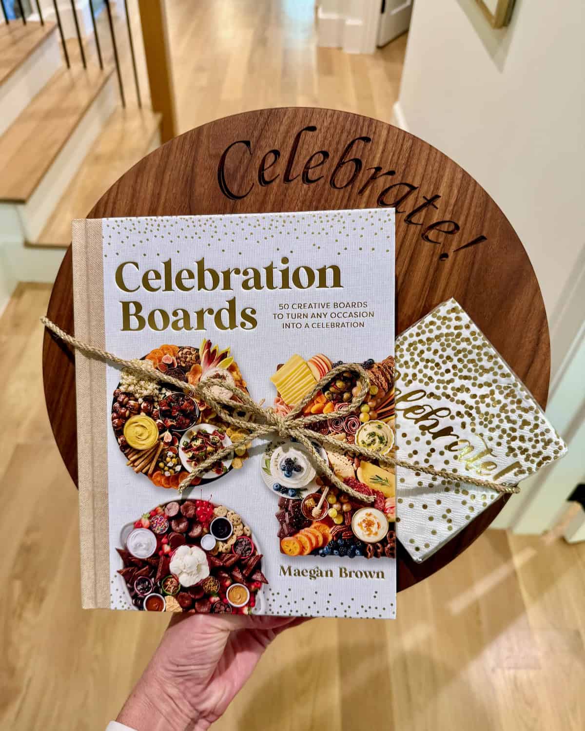 Celebration Boards cookbook paired with a round wood food board engraved with the word Celebrate.