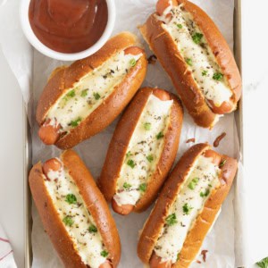 Six cheesy garlic bread hot dogs on a parchment lined aluminum baking sheet.