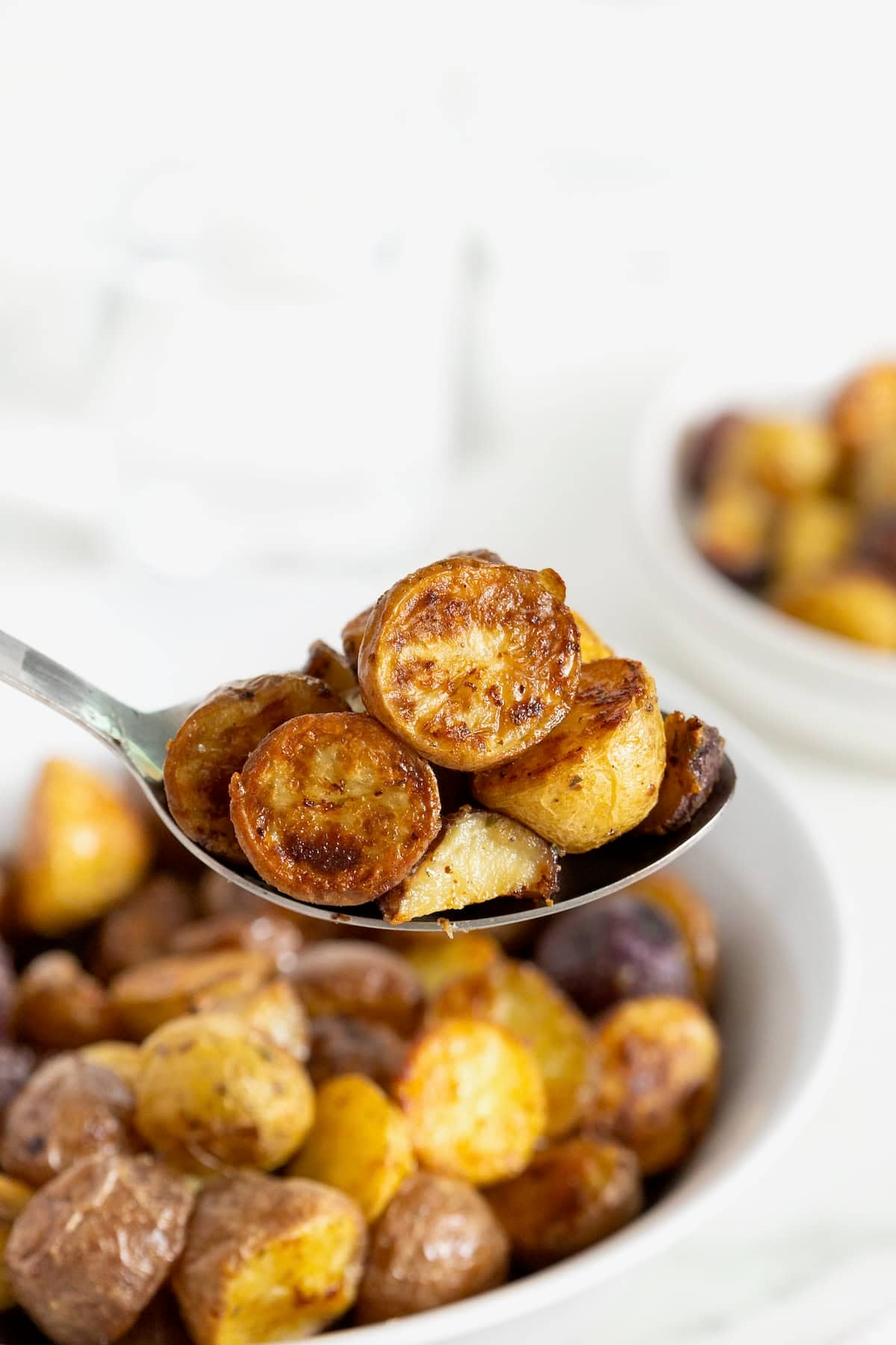 A serving spoon full of crispy ranch potatoes. A white bowl of potatoes is in the background.