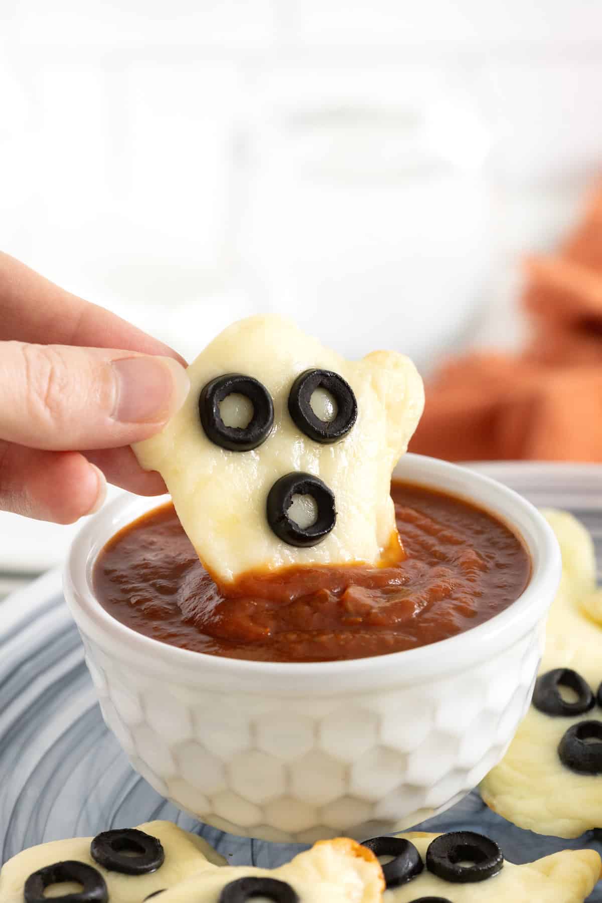 A Halloween Ghost Tortilla Pizza being dipped in marinara sauce in a white dish.