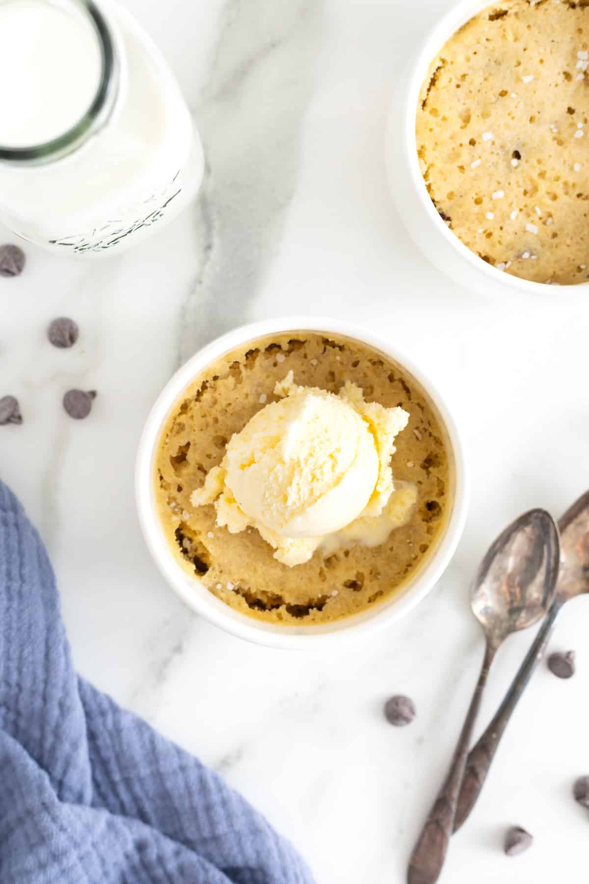 A scoop of vanilla ice cream on a microwave chocolate chip cookie in a white ramekin.