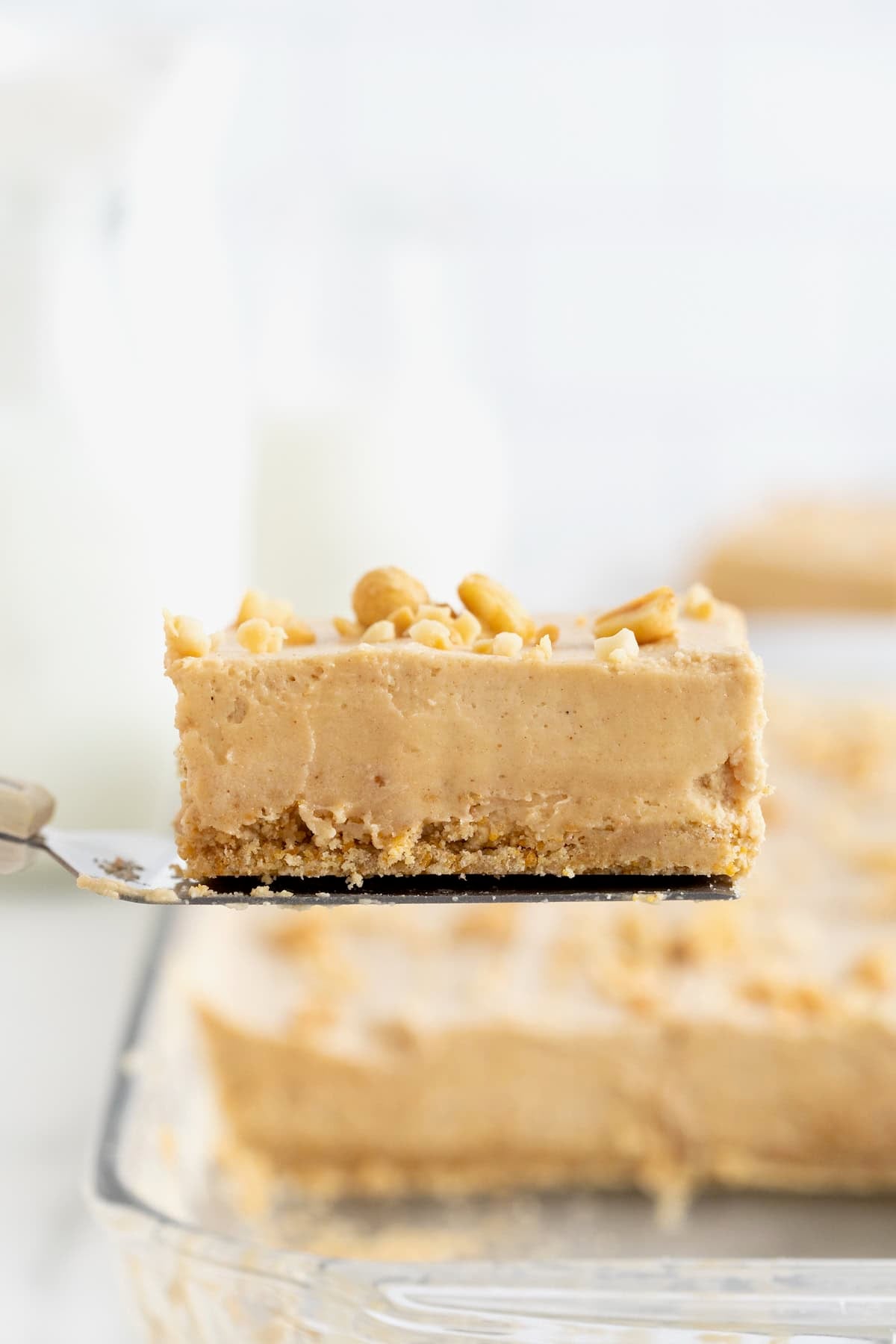 A no-bake peanut butter pie bar on a spatula. In the background is a glass dish of pie bars.