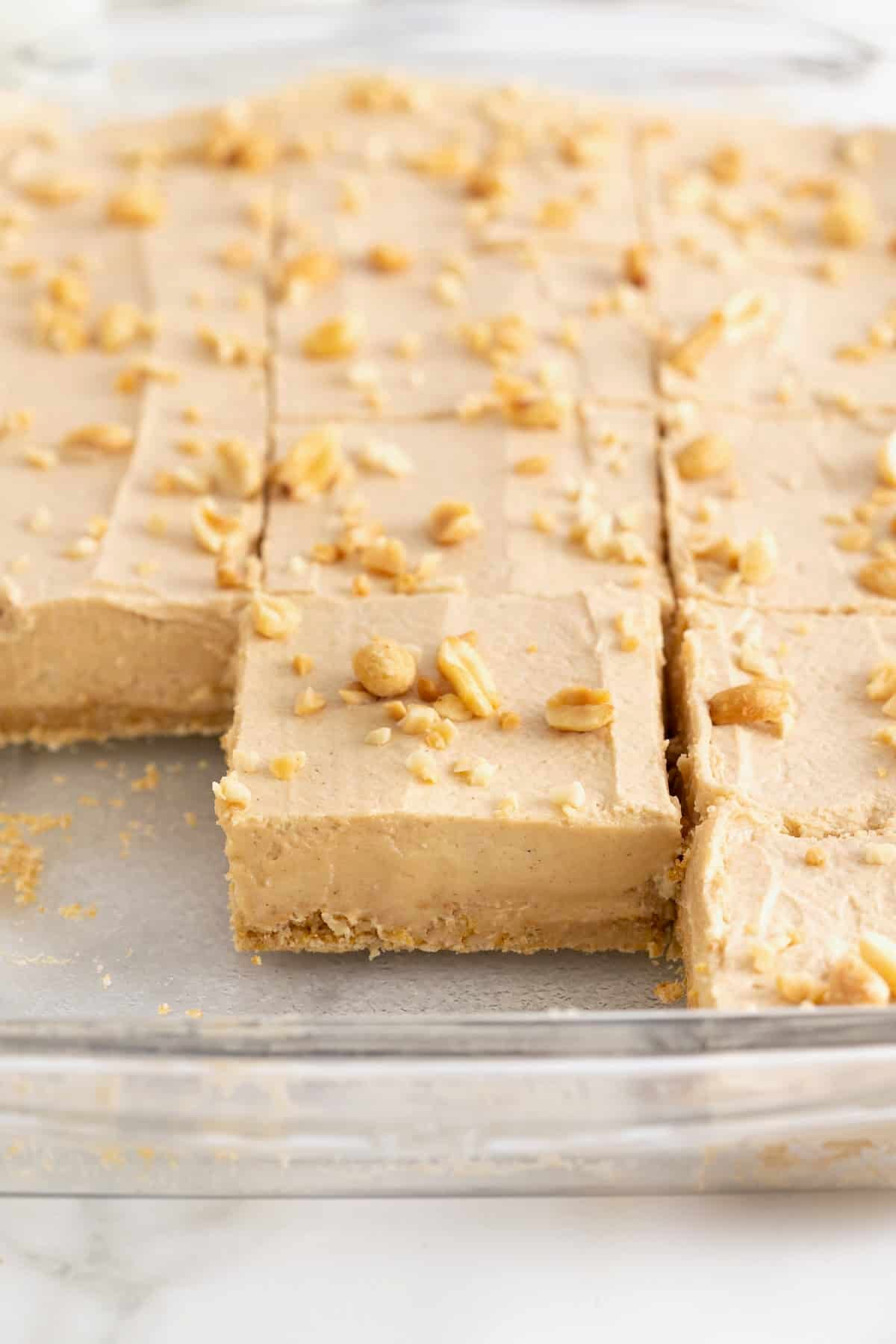 A glass dish of no-bake peanut butter pie sliced into squares. A few squares have been removed.