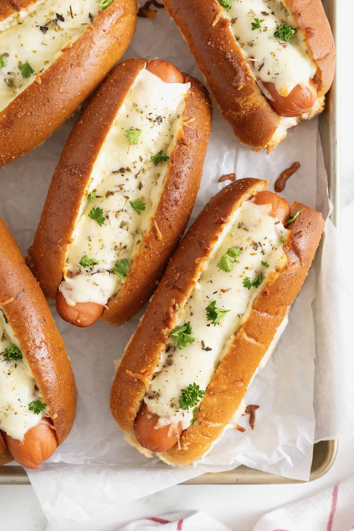 Six cheesy garlic bread hot dogs on a parchment lined aluminum baking sheet.