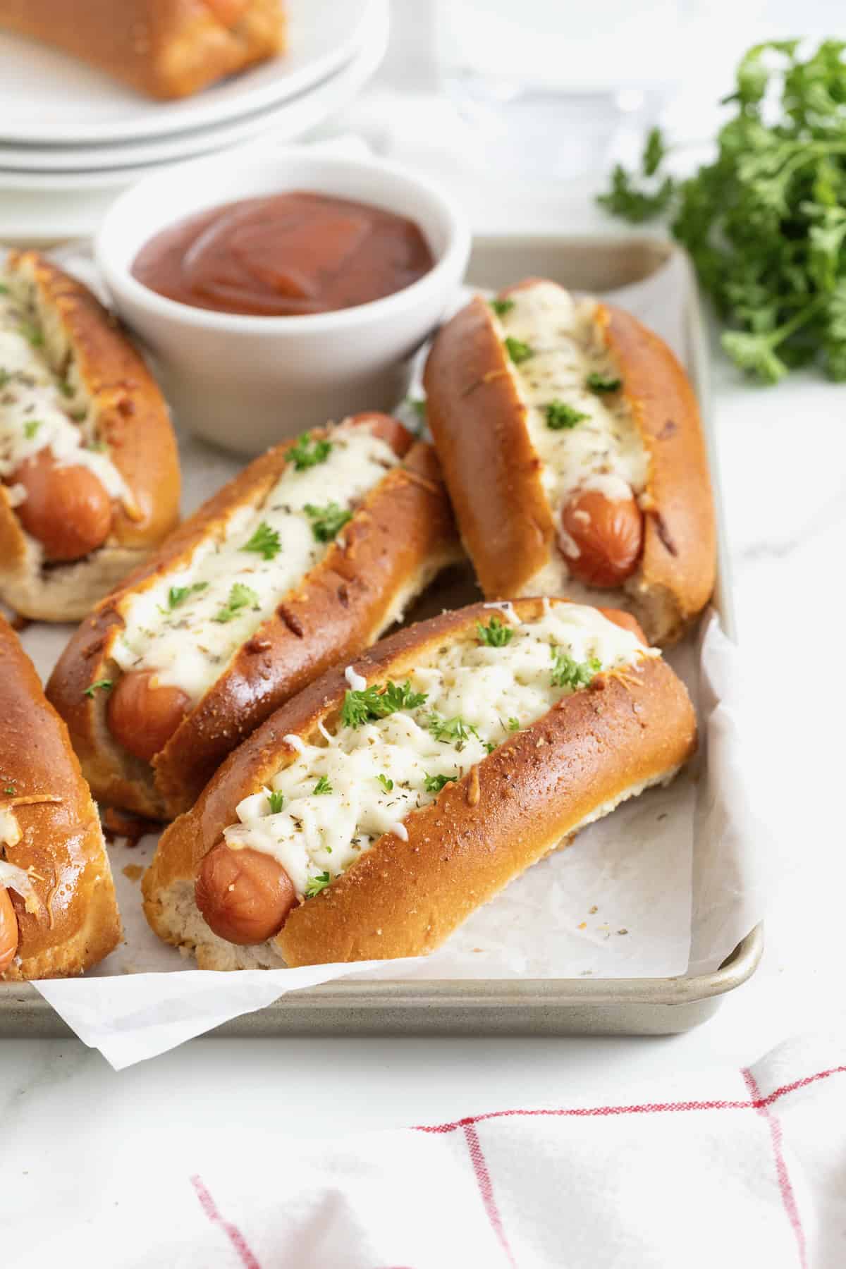 Six cheesy garlic bread hot dogs on a parchment lined aluminum baking sheet.