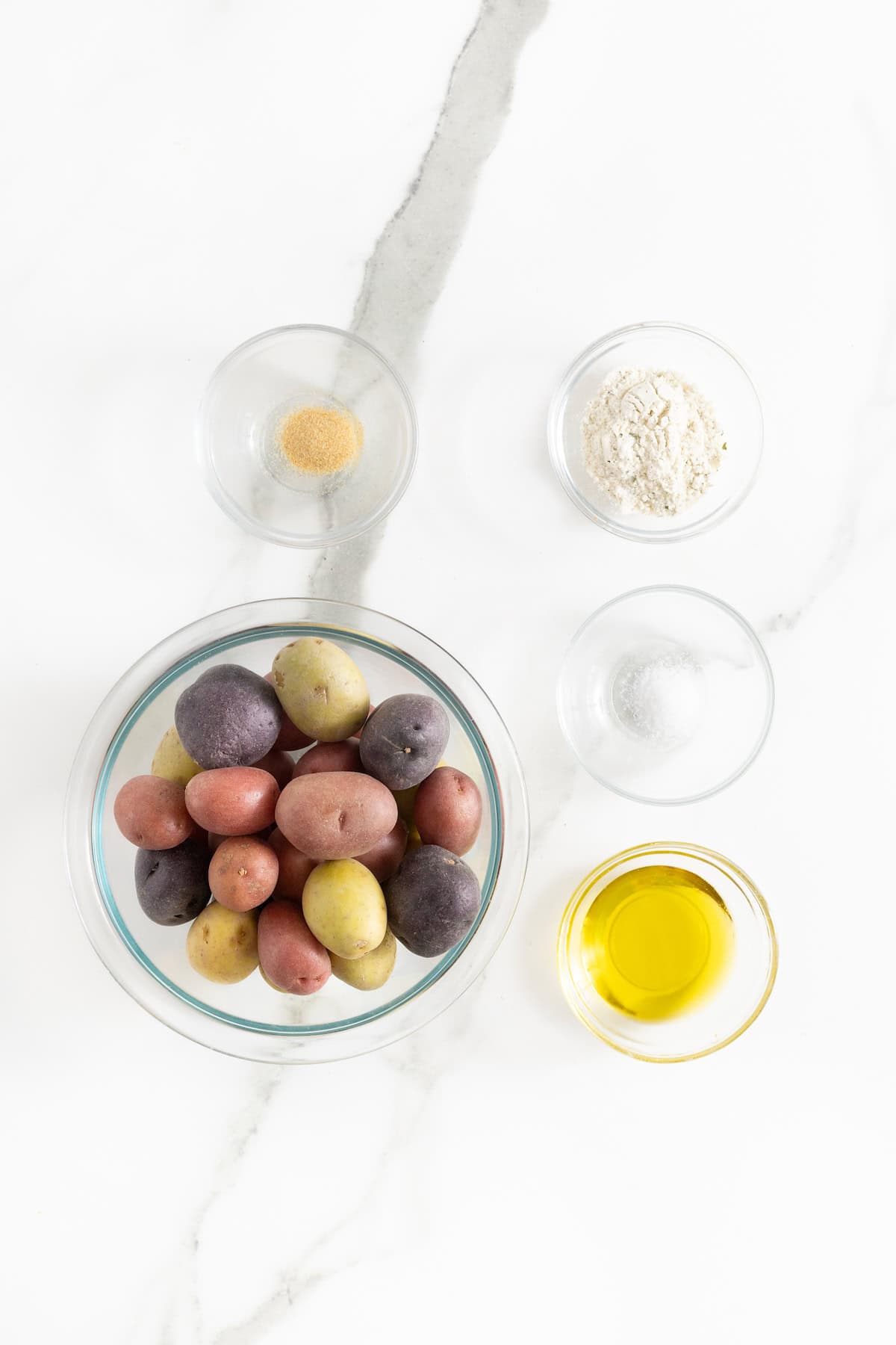 Ingredients to make crispy ranch roasted potatoes in glass dishes on a white marble counter.