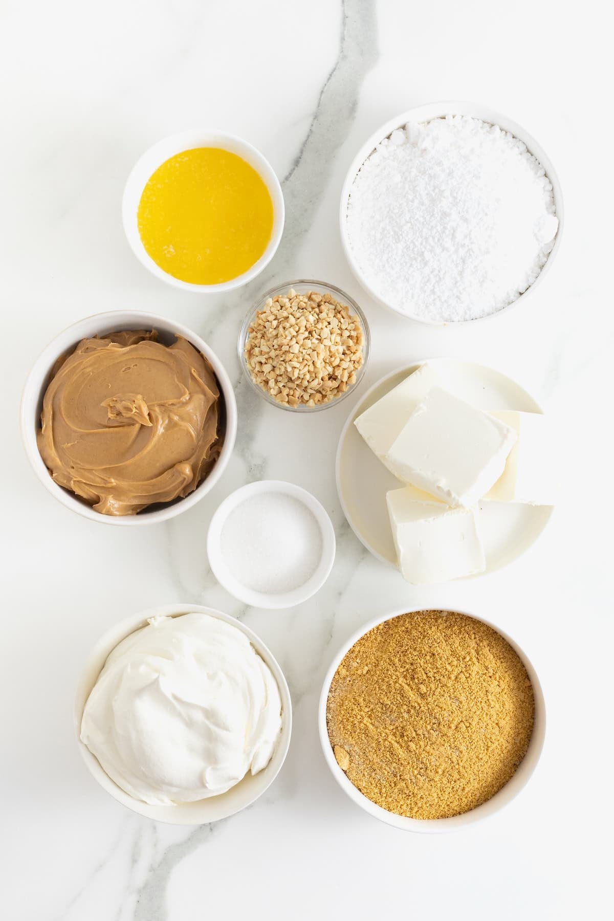 Ingredients to make No-Bake Peanut Butter Pie Bars in white dishes on a white and gray marble counter.
