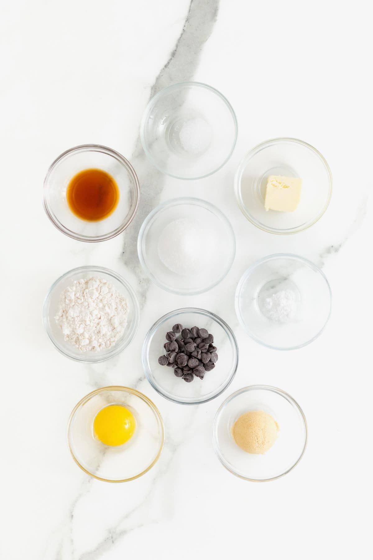 Ingredients to make a single-serve chocolate chip cookie in small glass dishes on a white marble counter.