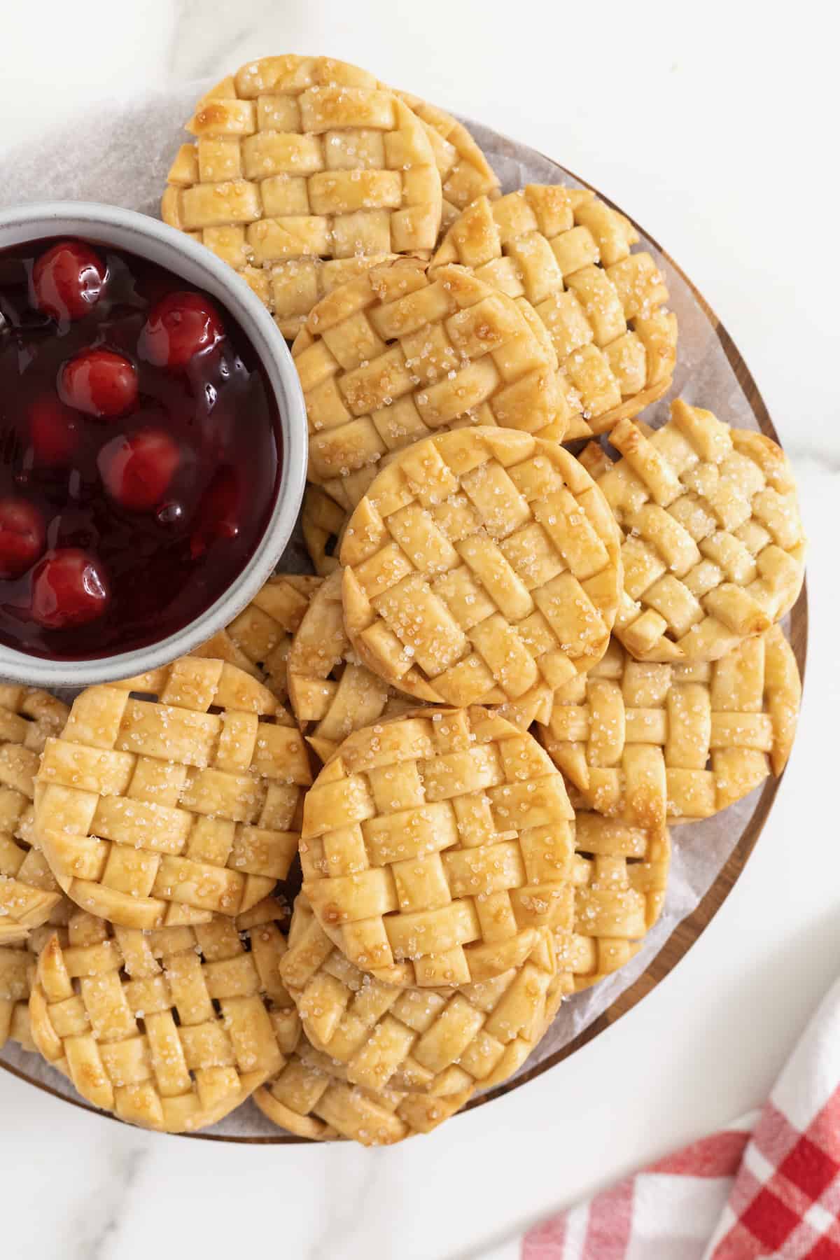Lattice pie cookies on a serving plate with a small white bowl of cherry pie filling.