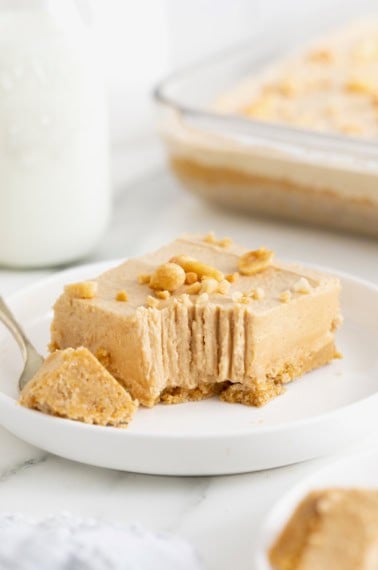 A no-bake peanut butter pie bar on a white dessert plate with a fork. A bite has been taken out of the bar.