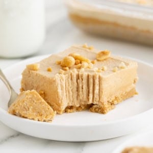 A no-bake peanut butter pie bar on a white dessert plate with a fork. A bite has been taken out of the bar.