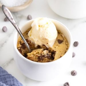 A microwave chocolate chip cookie in a white ramekin topped with a scoop of vanilla ice cream.