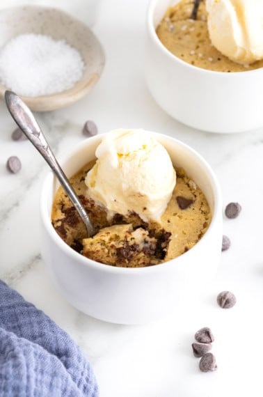A microwave chocolate chip cookie in a white ramekin topped with a scoop of vanilla ice cream.