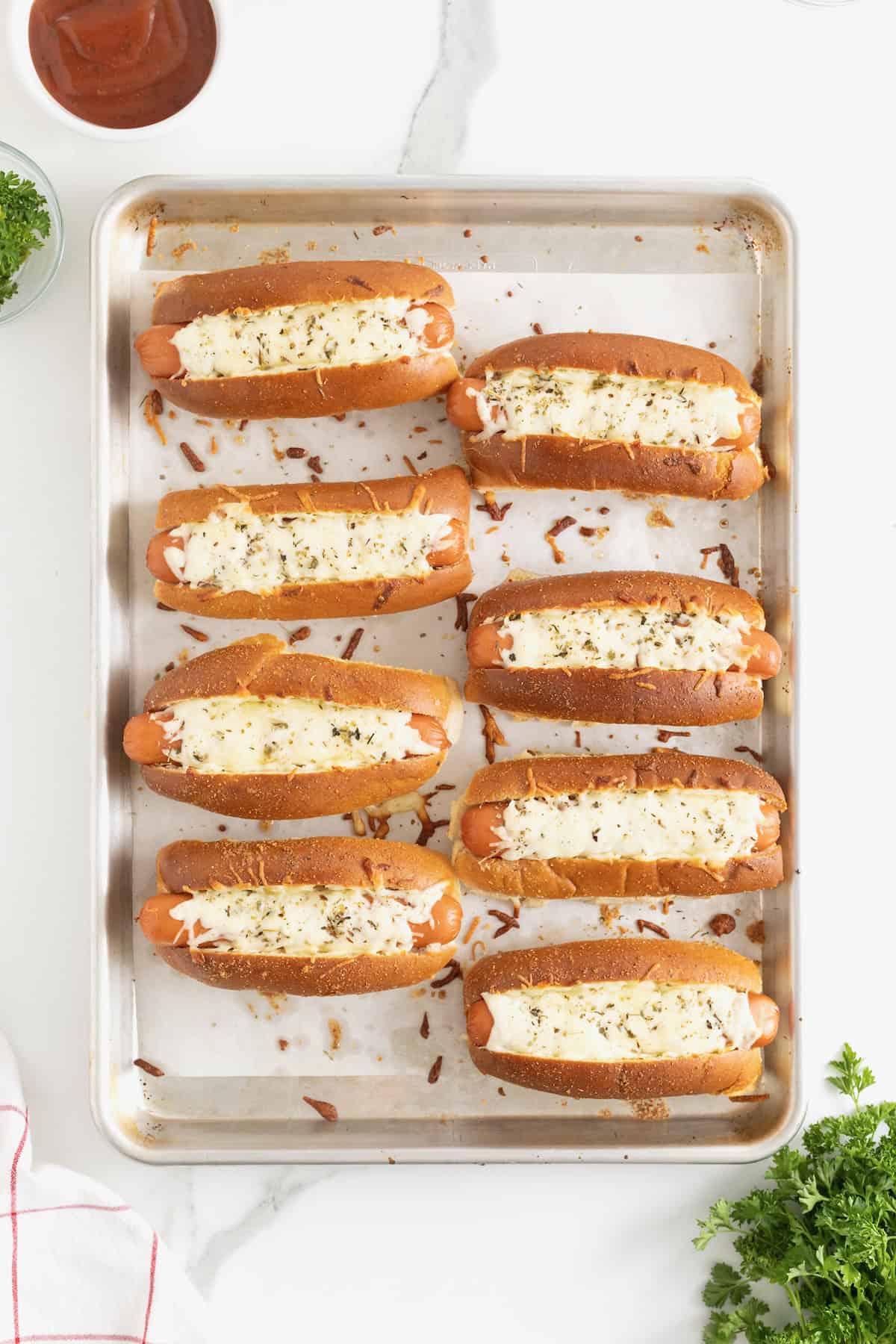 8 baked hot dogs with melted cheese on a parchment lined aluminum baking sheet.